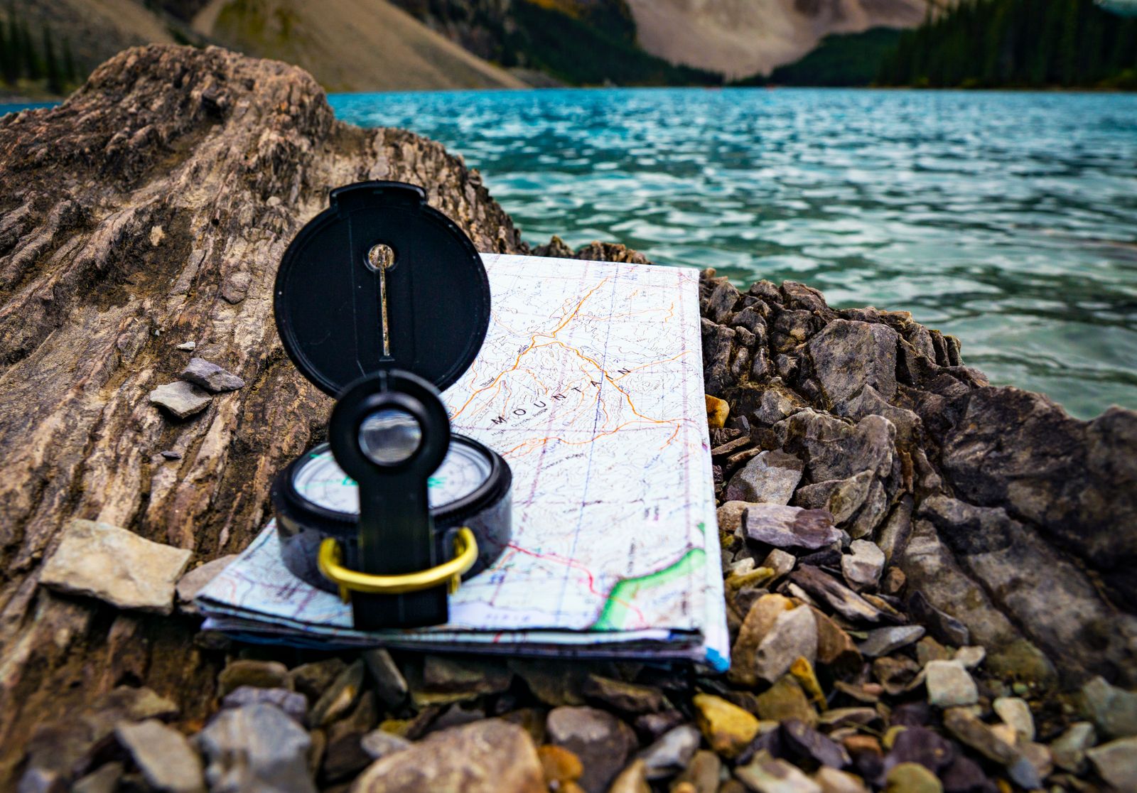 A baseplate compass resting on an open topographic map, its direction-of-travel arrow aligned with a ridgeline of brown contour lines.